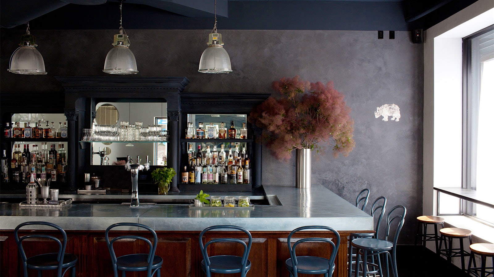The modern-design bar at Vinateria, with gray bistro chairs, a gray wall and a mirrored barback; a metal vase of pampas grass sits on the marble bar